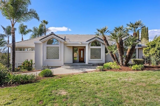 view of front of home with fence, a tiled roof, a front lawn, and stucco siding