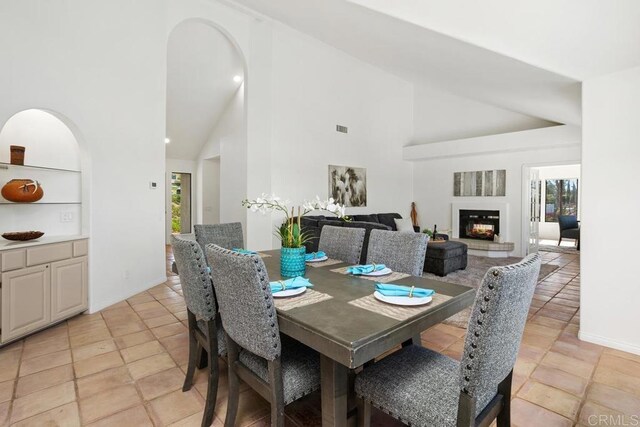 dining area with arched walkways, high vaulted ceiling, a glass covered fireplace, and visible vents