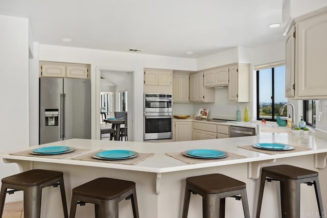 kitchen with a peninsula, a sink, visible vents, light countertops, and appliances with stainless steel finishes