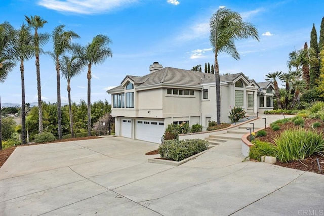 view of front of house featuring a garage, concrete driveway, a chimney, and stucco siding