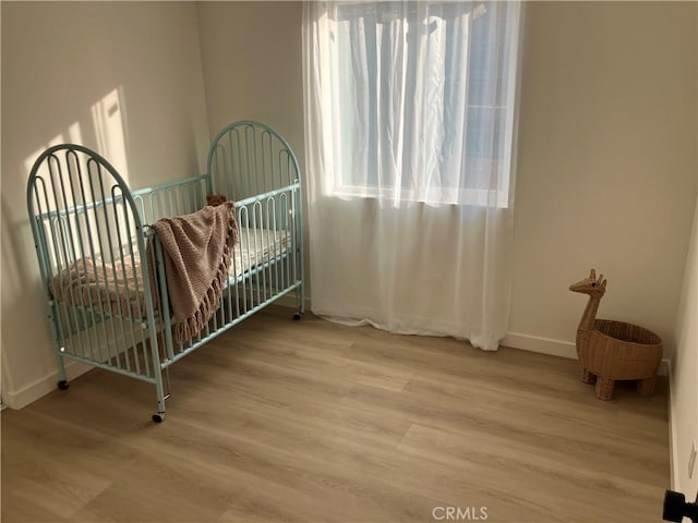 bedroom featuring a nursery area, light wood-style flooring, and baseboards