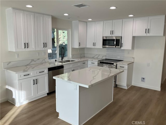 kitchen with visible vents, white cabinets, light stone counters, stainless steel appliances, and a sink