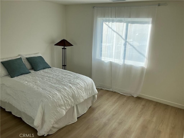 bedroom with baseboards, visible vents, and wood finished floors