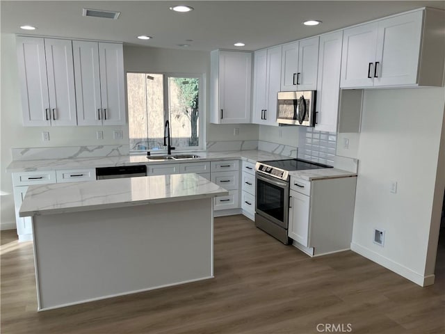 kitchen featuring visible vents, white cabinets, appliances with stainless steel finishes, light stone countertops, and a sink