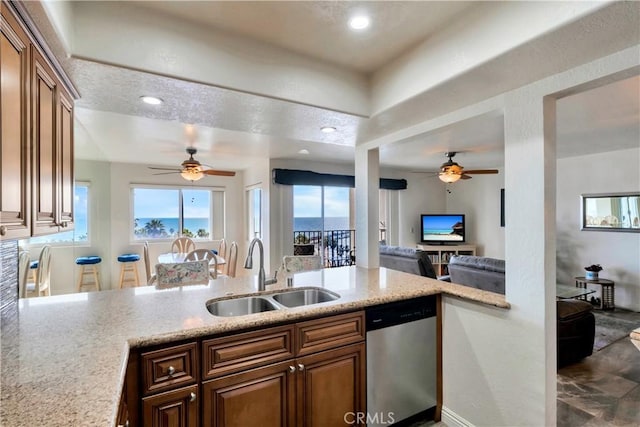 kitchen featuring light stone counters, a peninsula, a sink, open floor plan, and dishwasher