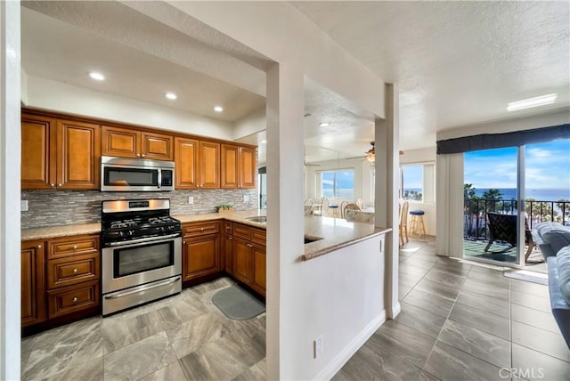 kitchen with stainless steel appliances, a textured ceiling, backsplash, a ceiling fan, and brown cabinetry