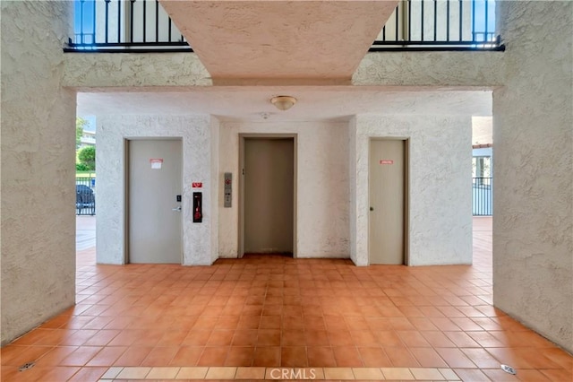 unfurnished room featuring a towering ceiling, elevator, tile patterned flooring, and a textured wall