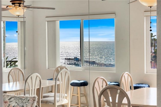 dining space with ceiling fan and a water view