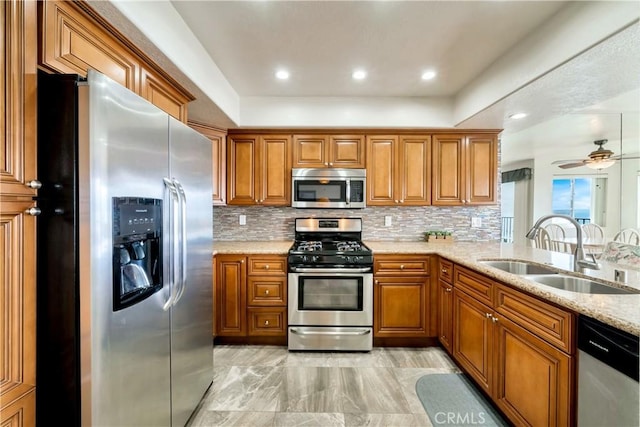 kitchen featuring brown cabinetry, decorative backsplash, stainless steel appliances, and a sink