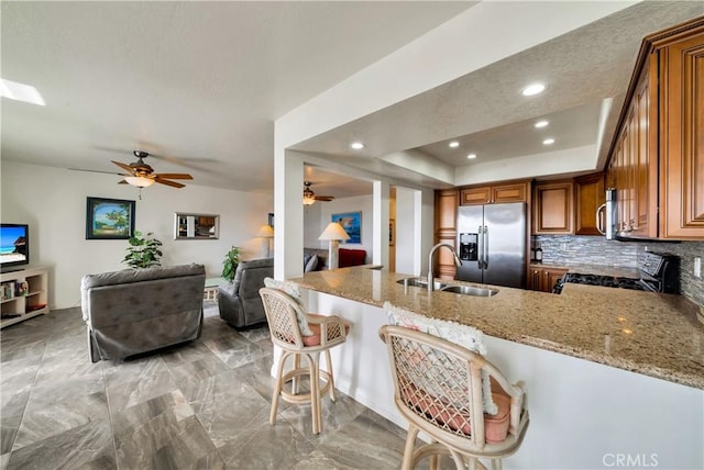 kitchen with brown cabinetry, light stone counters, stainless steel appliances, and a sink