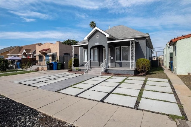 view of front of house featuring covered porch, roof with shingles, fence, and stucco siding