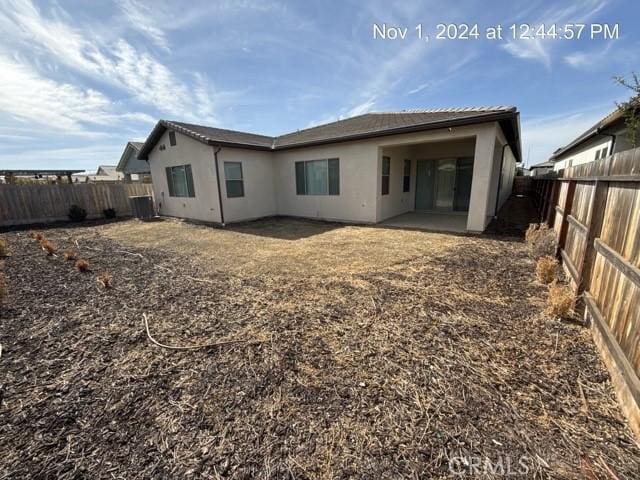 rear view of house with a fenced backyard, central AC, and stucco siding