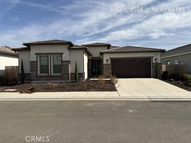 prairie-style house with stucco siding, an attached garage, fence, stone siding, and driveway