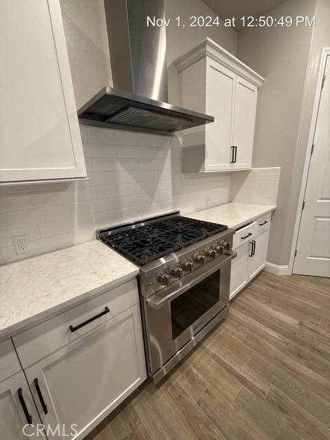 kitchen with decorative backsplash, white cabinets, wall chimney exhaust hood, dark wood-type flooring, and high end stove