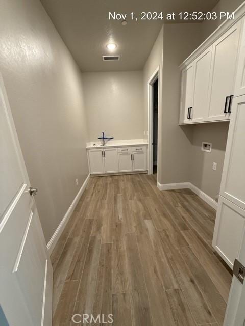 laundry room with hookup for a washing machine, wood finished floors, visible vents, baseboards, and cabinet space