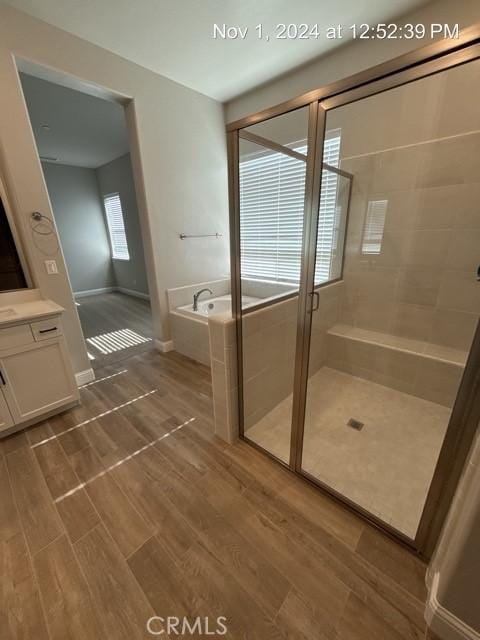 bathroom featuring a stall shower, baseboards, wood finished floors, a garden tub, and vanity