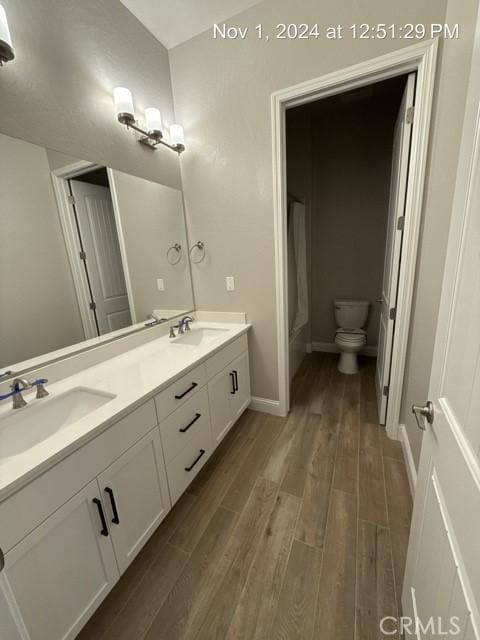 full bath featuring double vanity, a sink, toilet, and wood finished floors