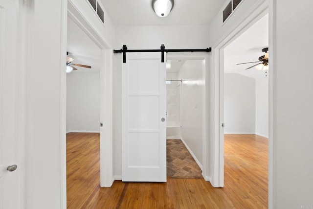 hall with visible vents, light wood-style flooring, baseboards, and a barn door