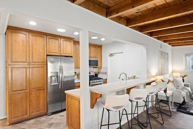 kitchen featuring stainless steel appliances, backsplash, light countertops, and a kitchen breakfast bar