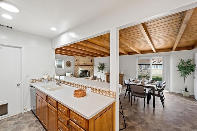 kitchen with a sink, visible vents, a brick fireplace, brown cabinets, and dishwasher