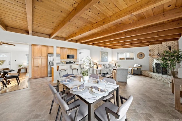 dining area with wooden ceiling, stone finish flooring, a brick fireplace, and beam ceiling