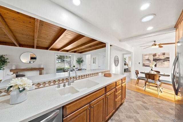 kitchen with brown cabinets, light countertops, stone finish flooring, a sink, and beamed ceiling