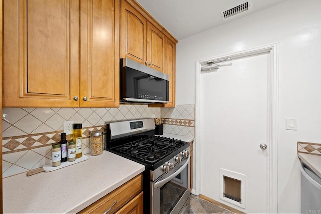 kitchen with tasteful backsplash, visible vents, brown cabinetry, appliances with stainless steel finishes, and light countertops