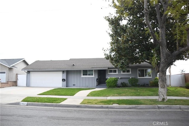 ranch-style home with a garage, fence, concrete driveway, a front lawn, and board and batten siding