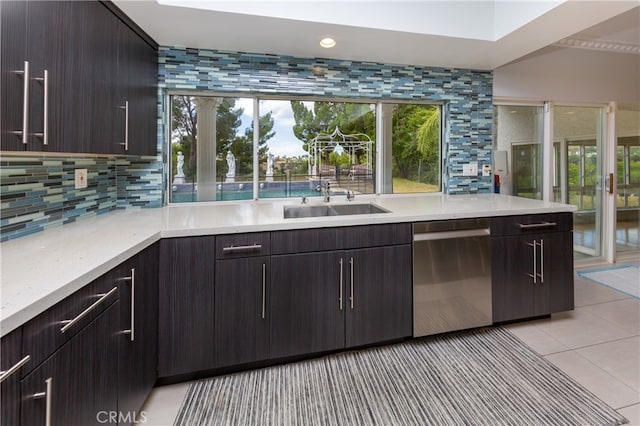 kitchen featuring decorative backsplash, dark brown cabinets, stainless steel dishwasher, a sink, and light tile patterned flooring