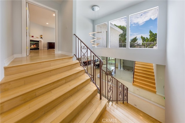 stairs with wood finished floors, a glass covered fireplace, and baseboards