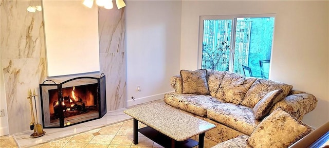 tiled living room with ceiling fan, a lit fireplace, and baseboards