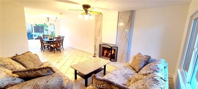 living room with a large fireplace, baseboards, and ceiling fan with notable chandelier