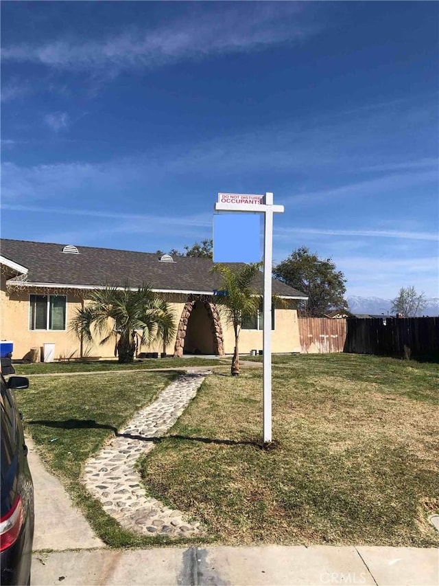 ranch-style home featuring stucco siding, a front lawn, and fence