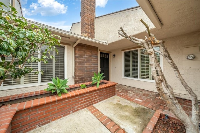 doorway to property featuring a chimney, a patio area, and stucco siding