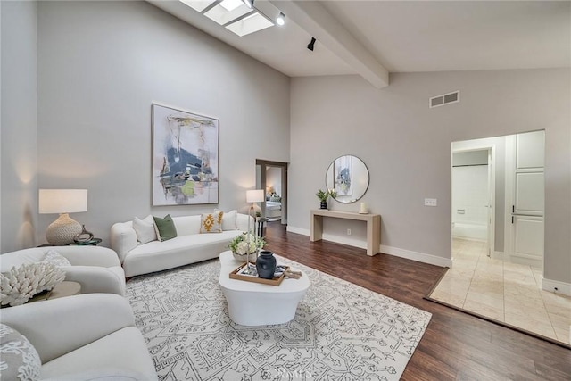 living area with a skylight, wood finished floors, visible vents, baseboards, and beamed ceiling