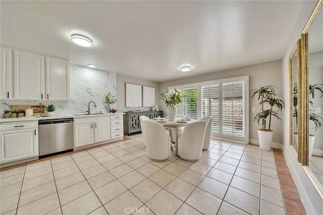 kitchen featuring light countertops, stainless steel dishwasher, white cabinetry, a sink, and light tile patterned flooring