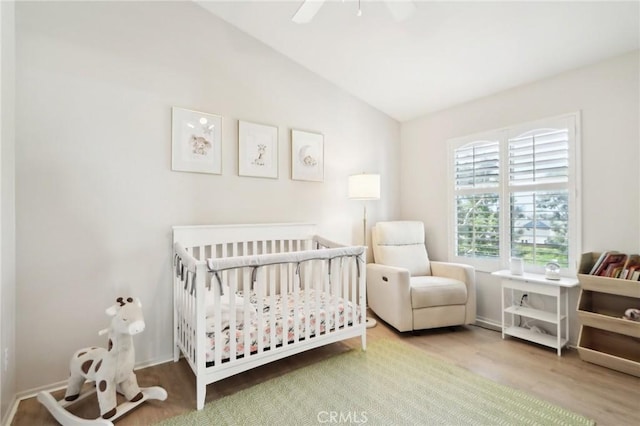 bedroom with lofted ceiling, ceiling fan, a crib, and wood finished floors