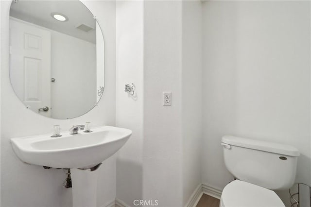 half bath featuring baseboards, a sink, and toilet