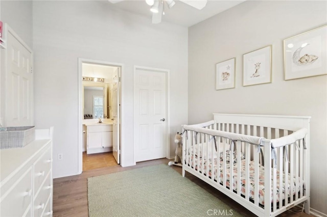 bedroom with a nursery area, wood finished floors, and a ceiling fan