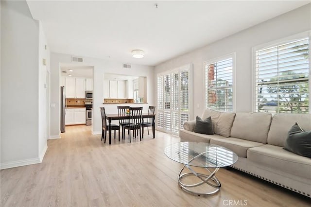 living area with light wood-style floors, visible vents, and baseboards