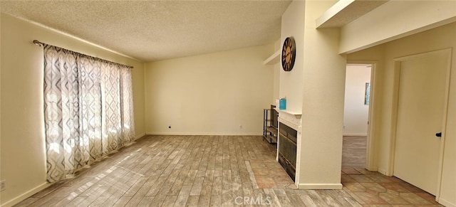 unfurnished living room featuring baseboards, light wood-style floors, a glass covered fireplace, and a textured ceiling