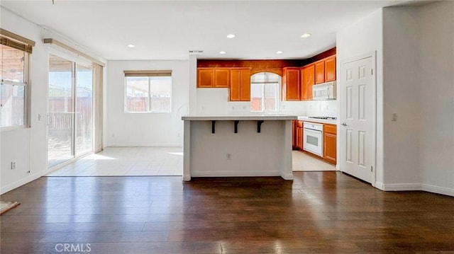 kitchen with light countertops, white appliances, wood finished floors, and brown cabinets