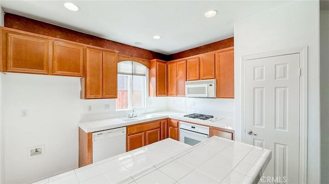 kitchen featuring tile countertops, recessed lighting, white appliances, a sink, and brown cabinetry