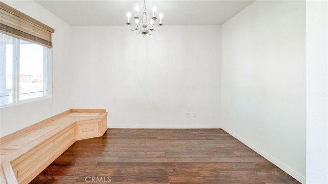 spare room featuring an inviting chandelier, baseboards, and dark wood-type flooring