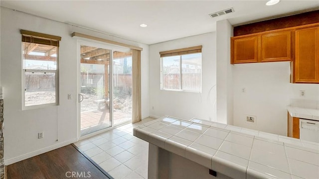 kitchen with tile countertops, brown cabinetry, visible vents, and baseboards