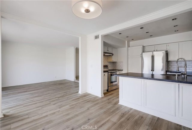kitchen with a sink, dark countertops, under cabinet range hood, appliances with stainless steel finishes, and tasteful backsplash