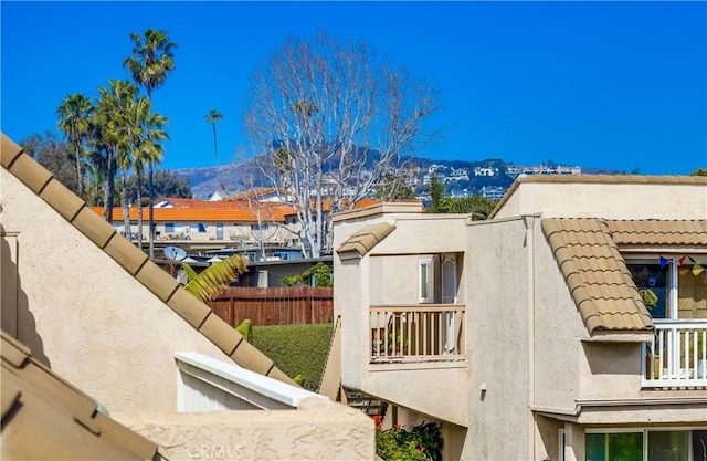 view of side of property with a tile roof, fence, stucco siding, and a balcony