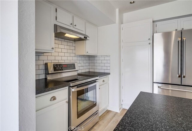 kitchen with under cabinet range hood, light wood finished floors, backsplash, dark countertops, and appliances with stainless steel finishes