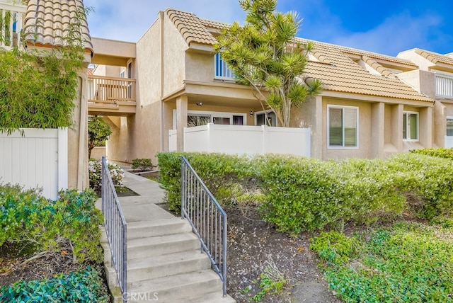 townhome / multi-family property featuring stairs, stucco siding, a tile roof, and fence