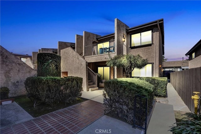 view of front of home featuring fence, a balcony, and stucco siding